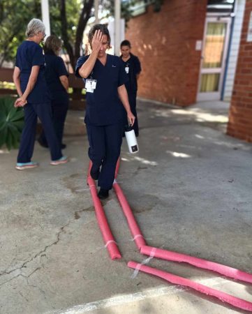 a nurse walks a path outlined with pink pool noodles. She has her hand over one eye.