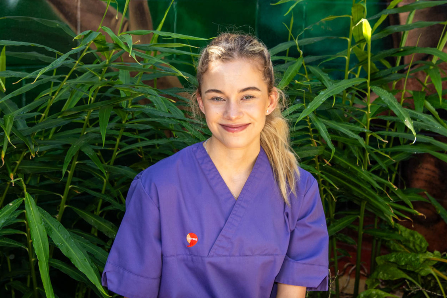 A nurse in a purple uniform smiling in a garden.