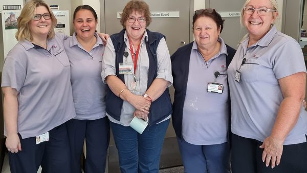Five women wearing pale purple shirts standing closely together.