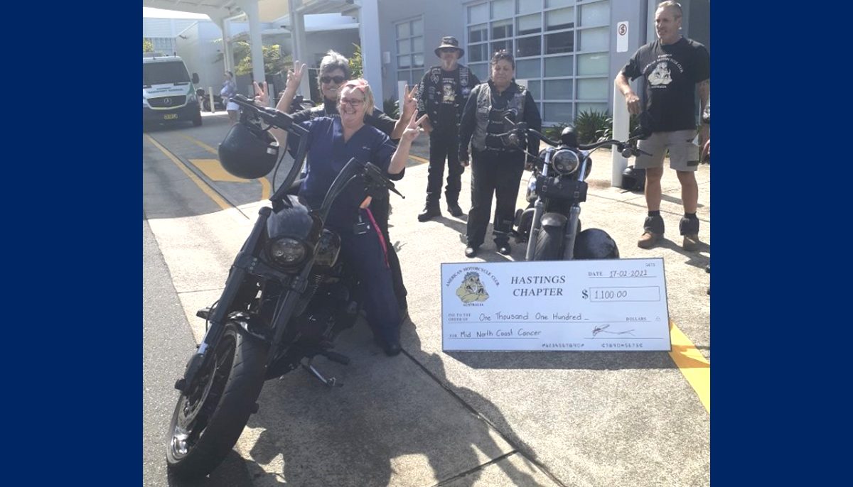 two motorcycles at the front of a hospital building with riders and a big cheque. Also present is a nurse sitting on the bike,