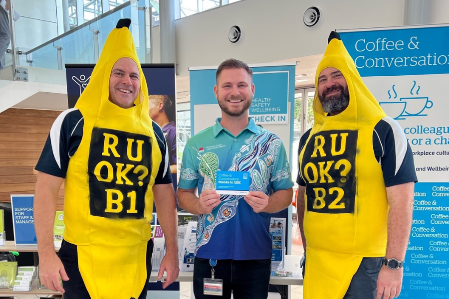 Two men dressed as bananas with a man holding a card.