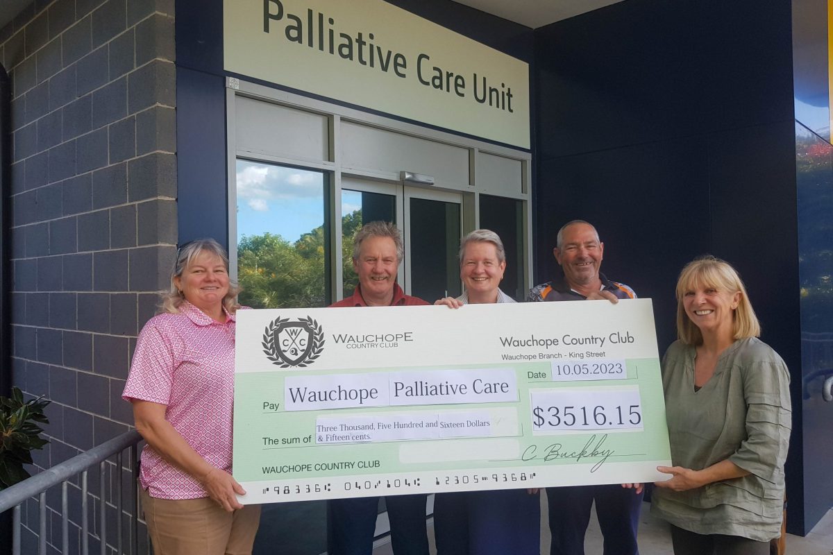 Five people standing together holding a big cheque outside a hospital.