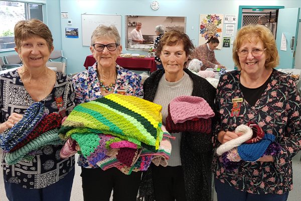 four women holding knitted rugs and beanies