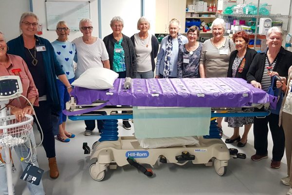 Twelve women stand around a hospital bed.