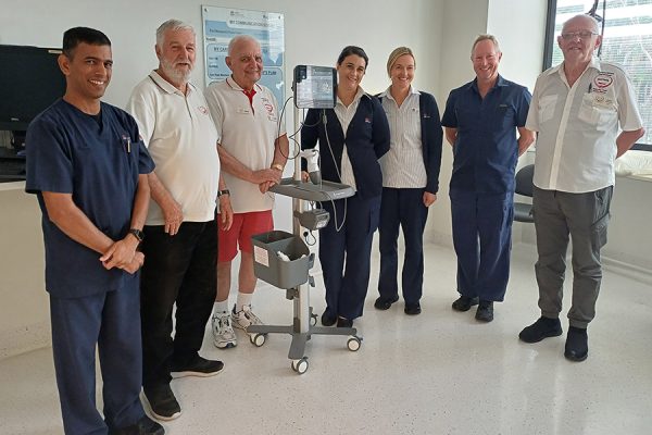 Seven people standing either side of a bladder scanner on a stand.