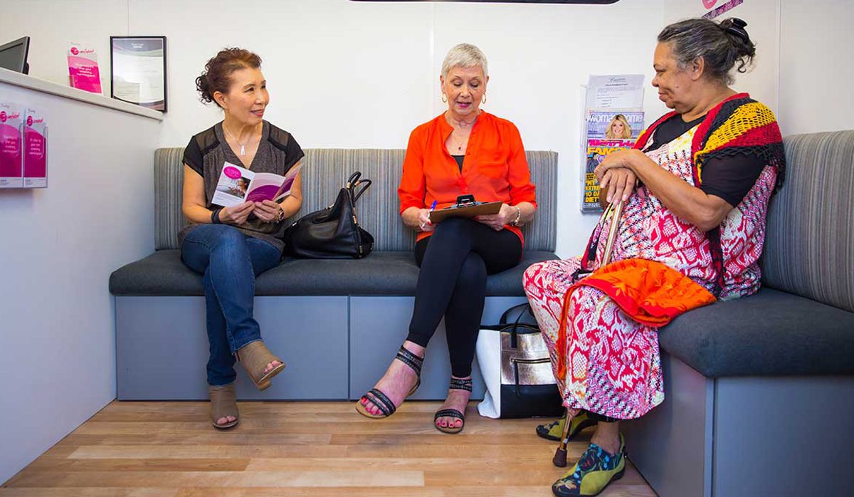 three women sitting on a lounge, one filling out a form on a clip board.