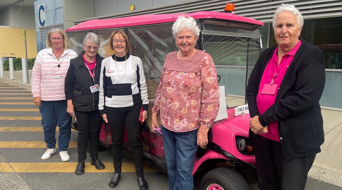 five women standing in front of a pink e-car at a hospital