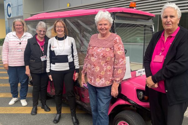 five women standing in front of a pink e-car at a hospital