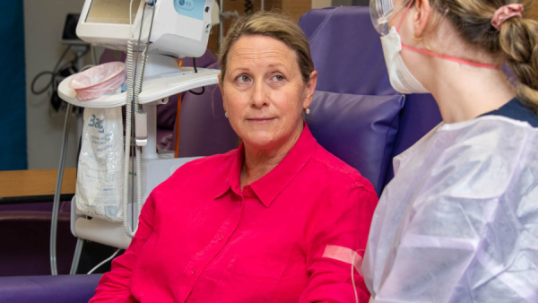 A woman in a chair speaking with a healthcare worker while receiving chemotherapy.