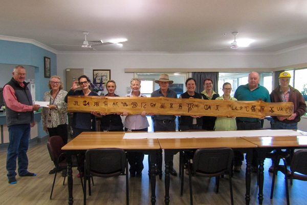 A group of people holding a long slab of timber in which farm brands have been burned.