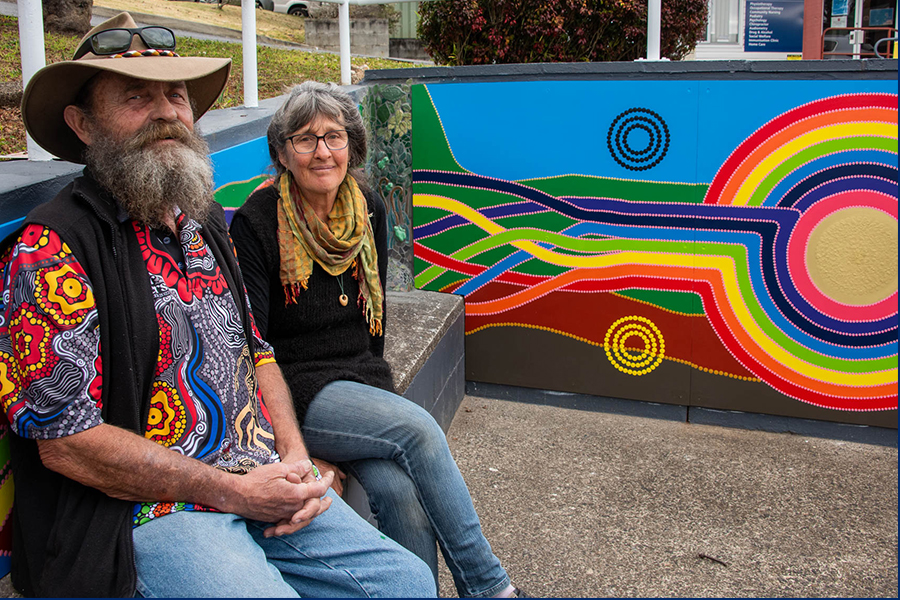 A man and a woman sitting next to each other next to a colourful rainbow mural