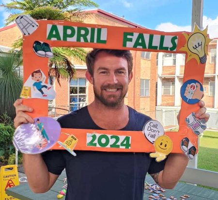 a male nurse holding an orange cardboard picture frame featuring the words April Falls 2024