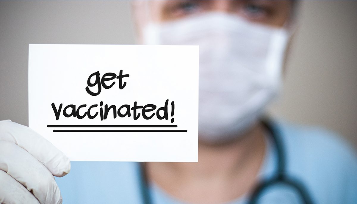 nurse holding a card that reads Get Vaccinated