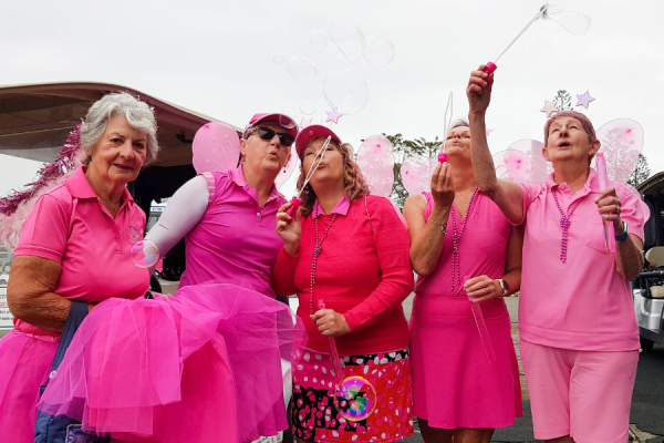 Women dressed in pin outfits and fairy wings with bubble wands for a charity golf event.