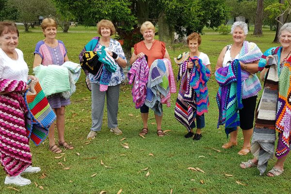 seven women holding rugs while standing in a grassed area