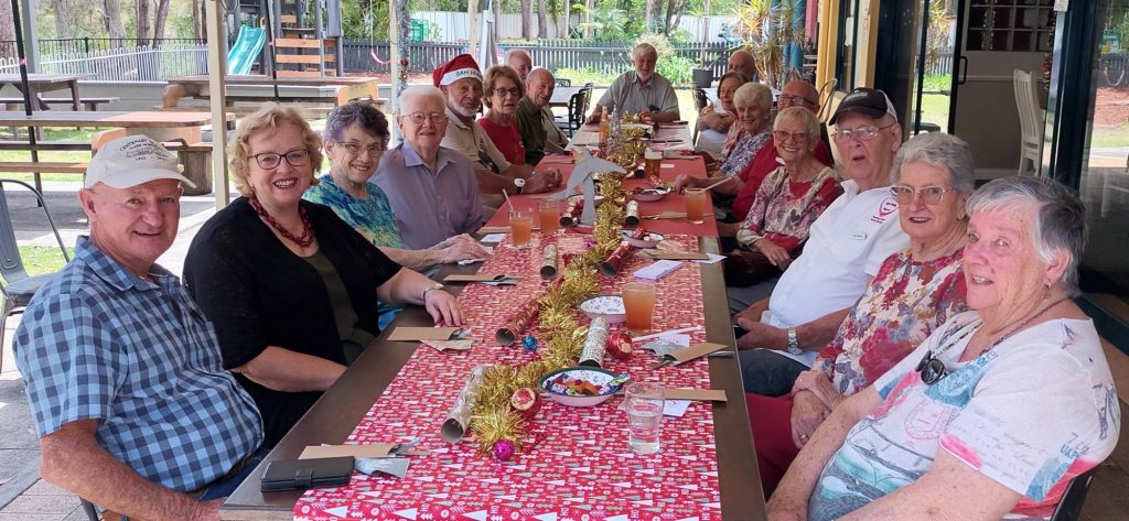 a group of older people sitting at a very long table decorated with Christmas bon-bons and tinsel