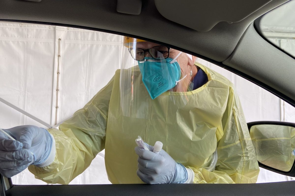 Close-up image of nurse in PPE testing a person in a car