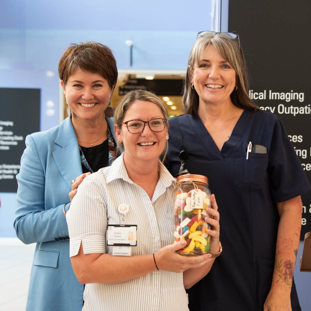 Three nurses smiling, one holding a jar of sweets.