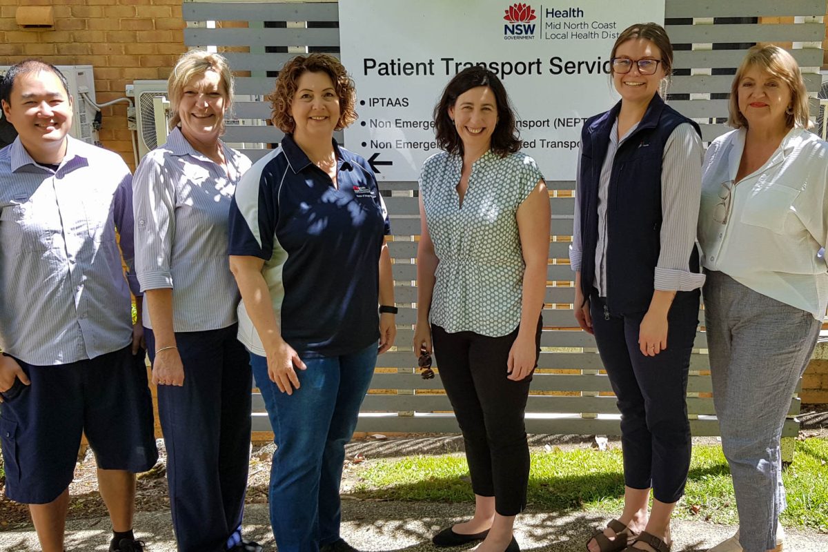 six people standing in front of a sign which reads patient transport services