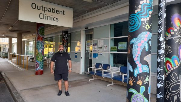 A man standing outside a hospital next to artwork he created on a concrete pole.