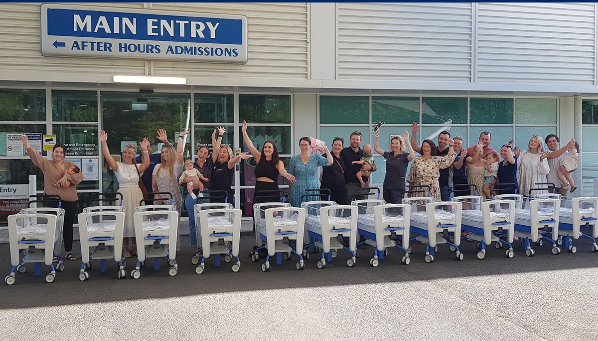 People standing behind 11 cots in front of a hospital