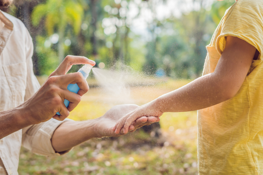 A parent holding the hand of a child as they spray them with mosquito repellent.