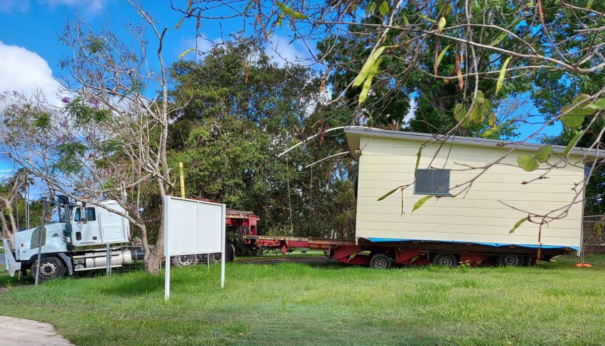 weatherboard building on the back of a semi-trailer being removed from a large block of land