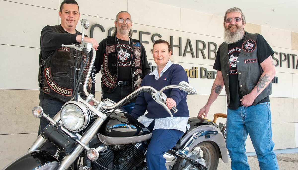 Three bikies and a Harley Davidson outside Coffs Harbour hospital. Sitting on the bike is a nurse.