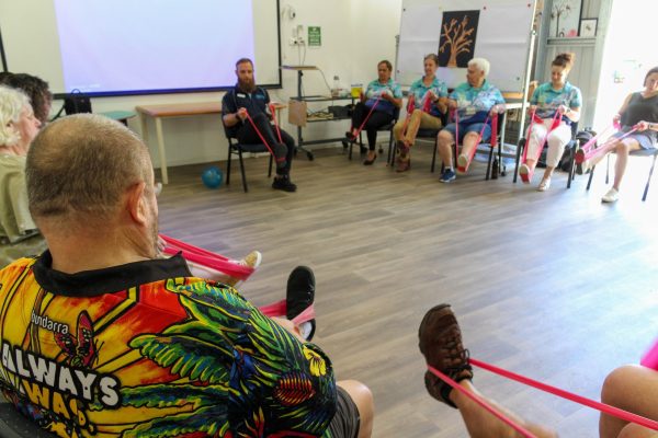 A group of people, seated on chairs using stretchy bands for exercise.