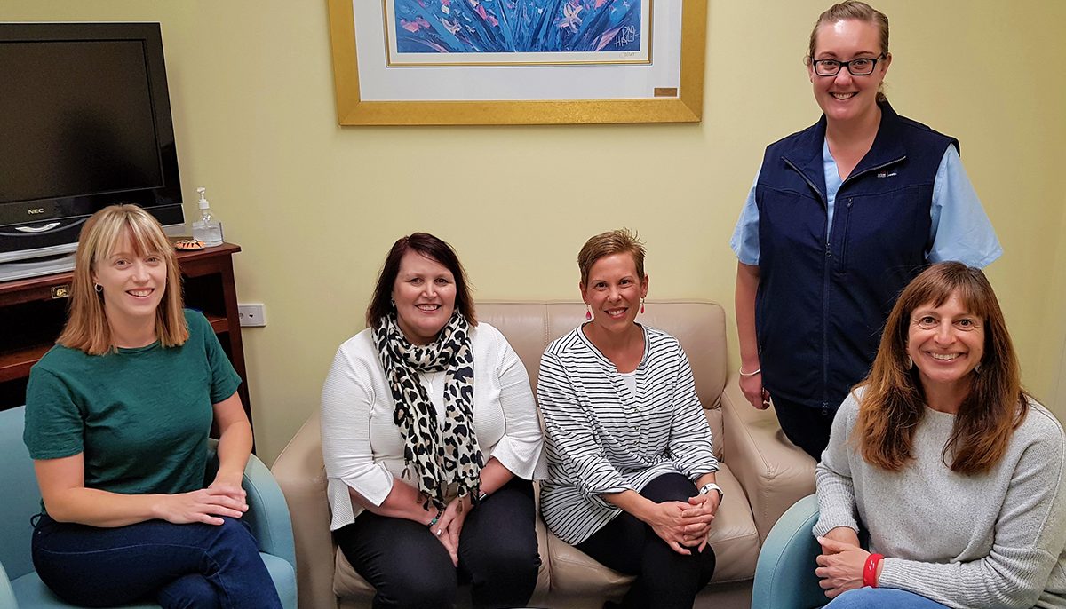 Four charity volunteers with cancer unit manager in quiet room used to support patients