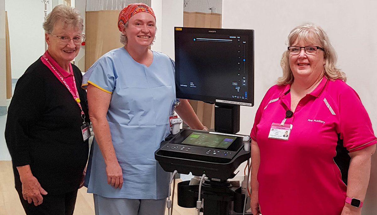 two hospital volunteers standing either side of an ultrasound and a nurse