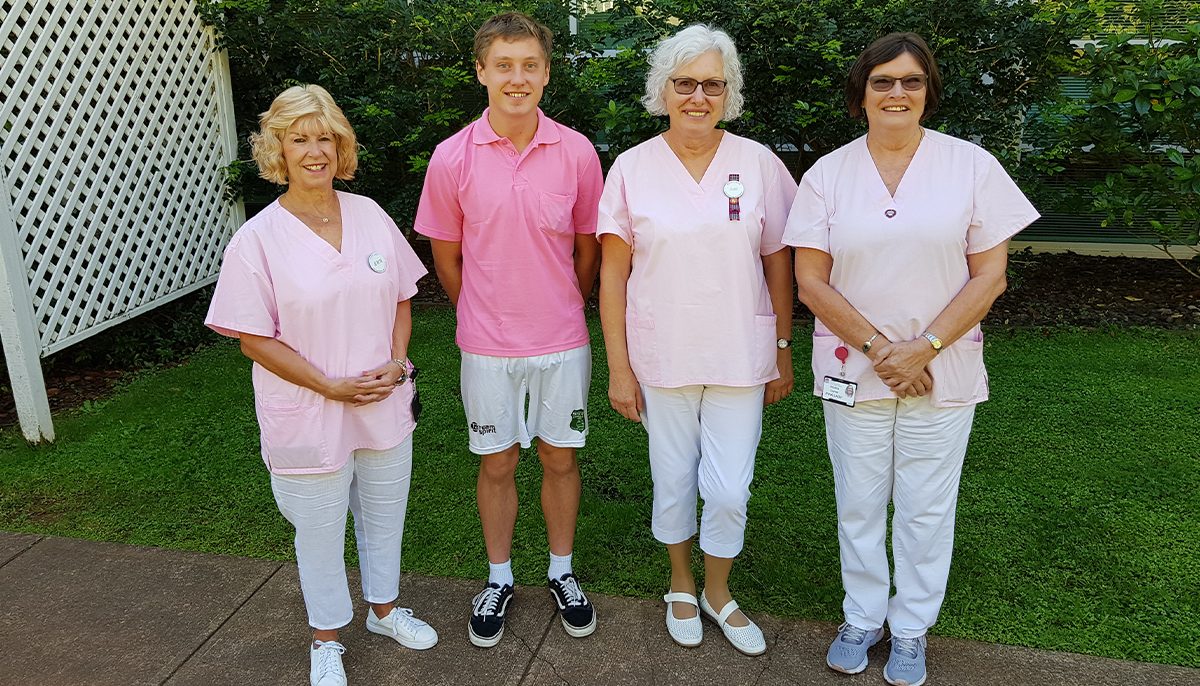 Four people wearing pink shirts standing together outside a hospital.