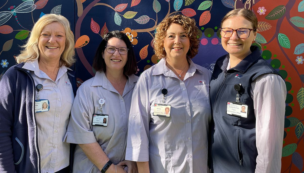 Four women in NSW Health uniforms standing in front of a colourfully painted wall