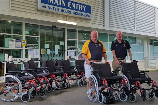 two men standing with 8 wheelchairs in front of a hospital