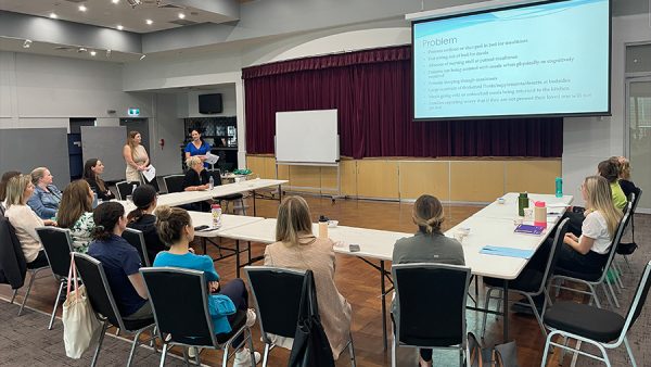 a group of health professionals sitting at a table in front of a large projector displaying professional development information.