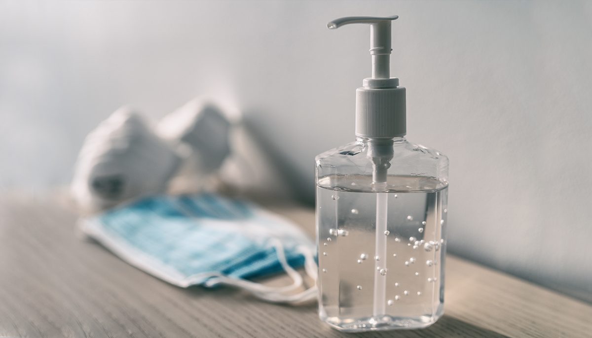 Image of hand sanitiser in bottle and disposable face mask in background