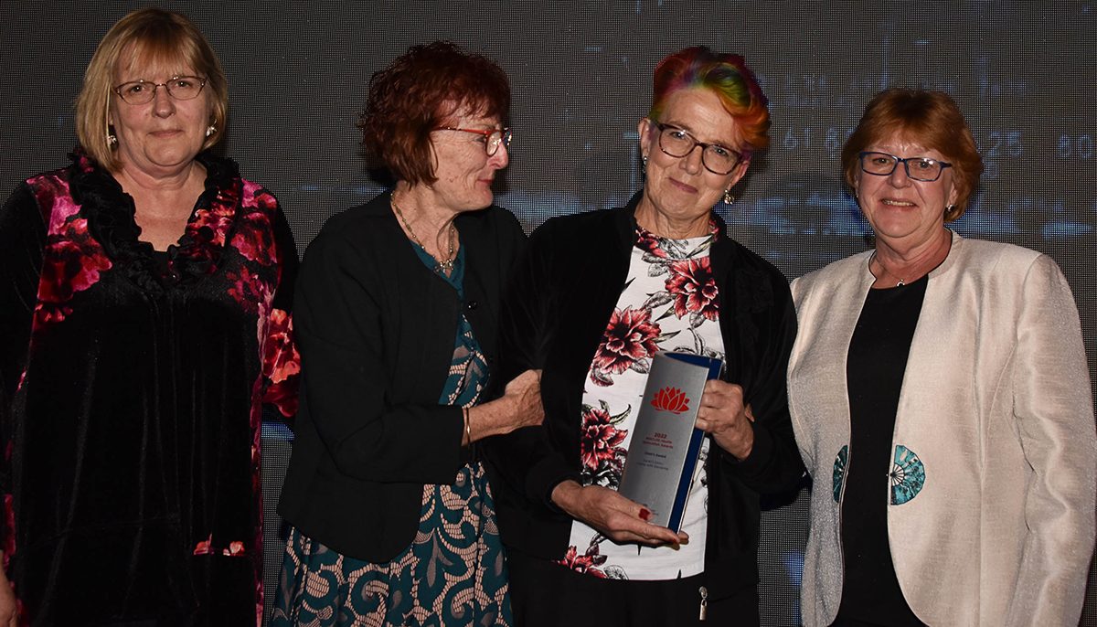 four women on stage, one holding an award