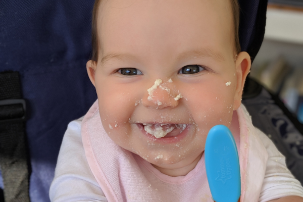 Baby with food on their face, holding a spoon.