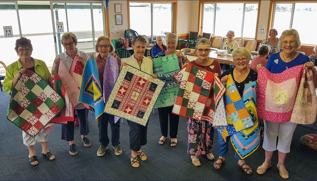 a group of women holding baby quilts, some with Christmas designs