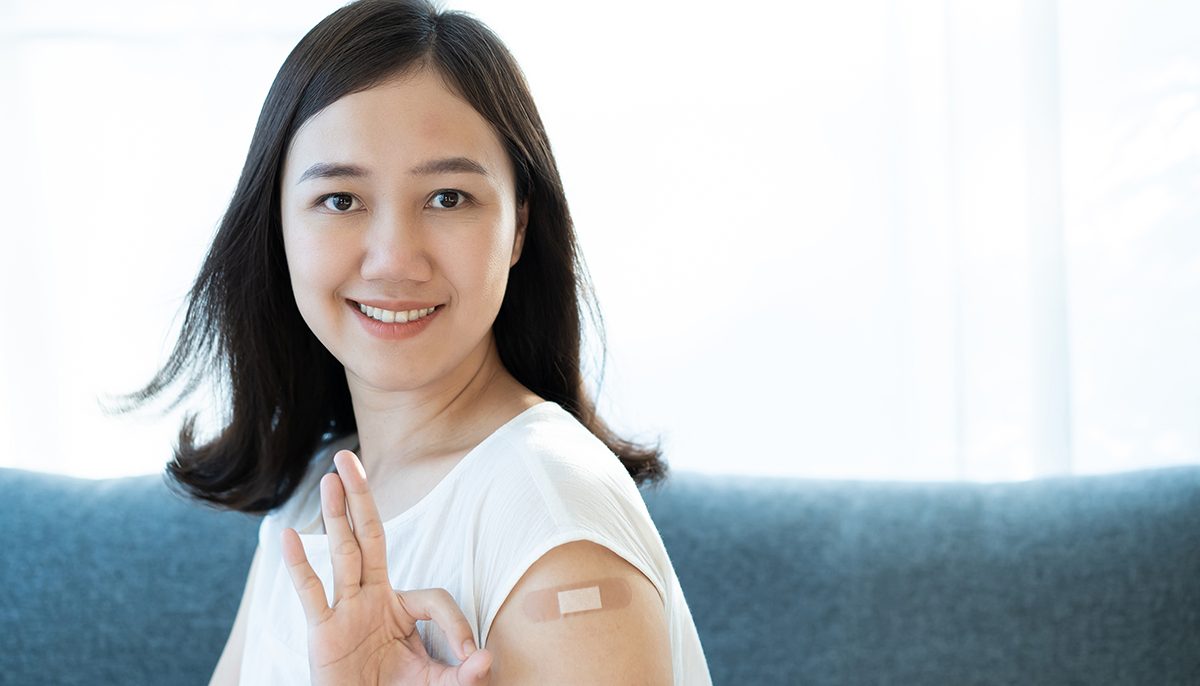 Photo of woman with band-aid on arm holding up three fingers.