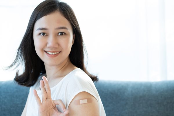 Photo of woman with band-aid on arm holding up three fingers.