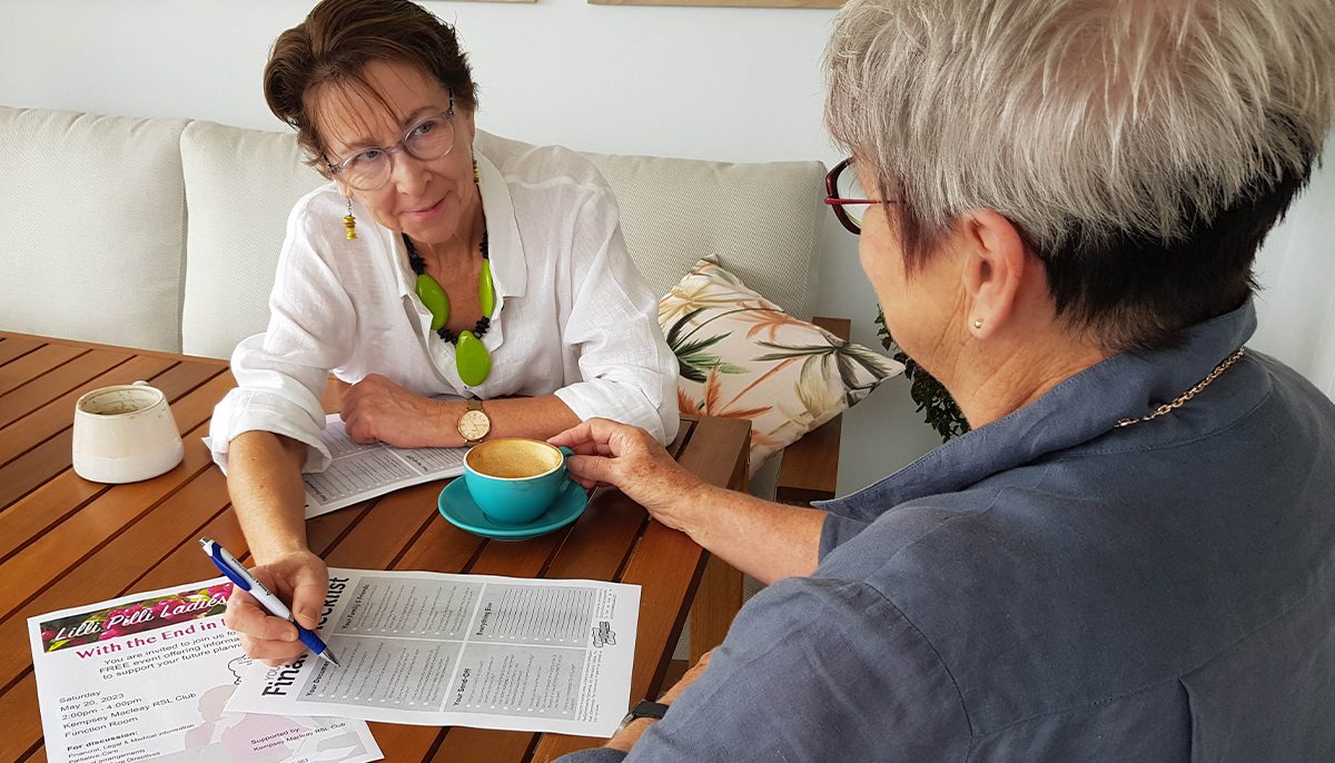 Two women talking to each other while looking at a flyer and a questionnaire on end-of-life issues.