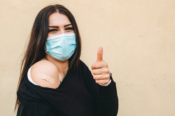 Young woman with thumbs up after vaccination